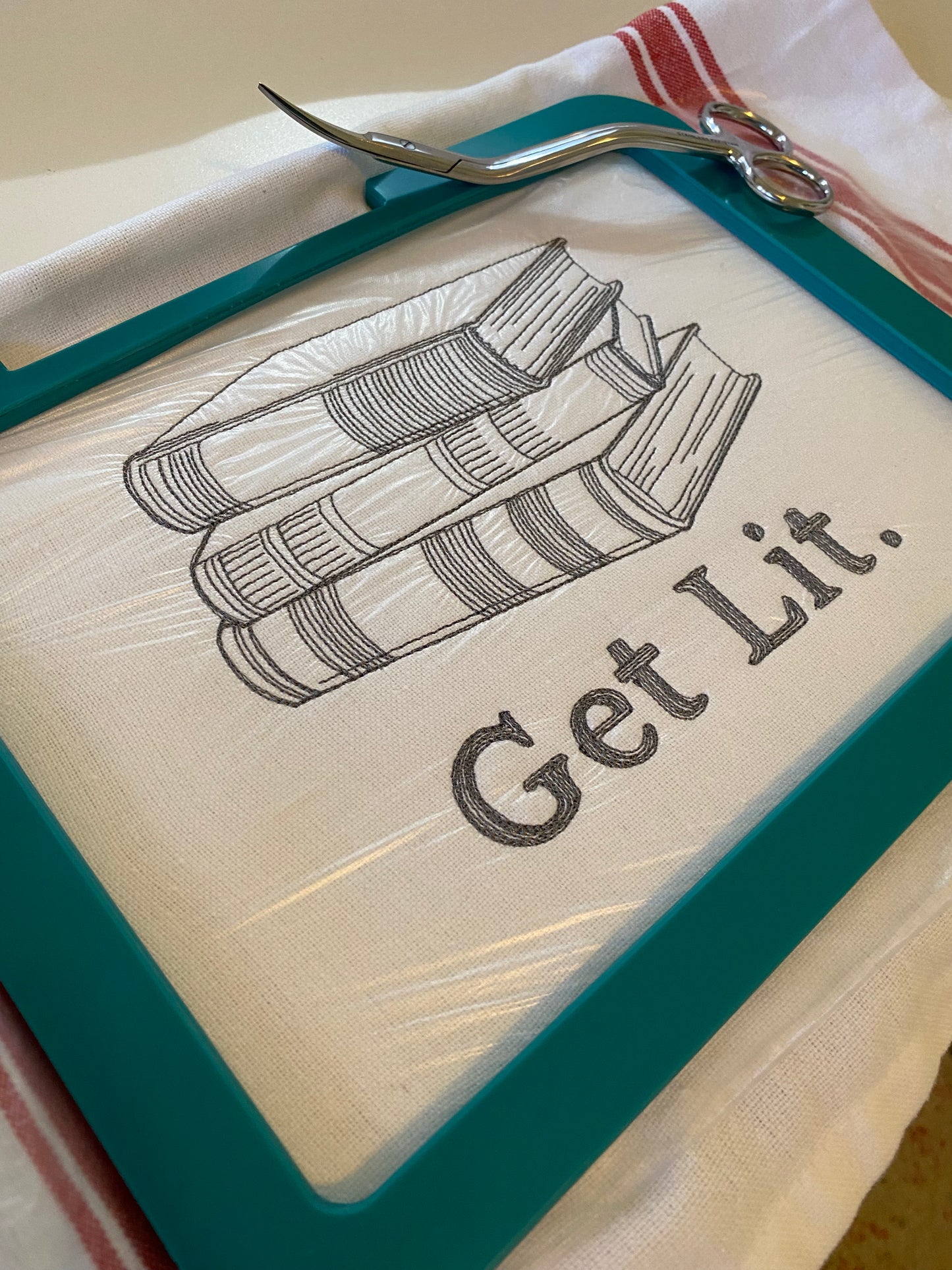 100% cotton tea towel featuring the phrase, “Get Lit” alongside a stack of books. embroidered in gray.